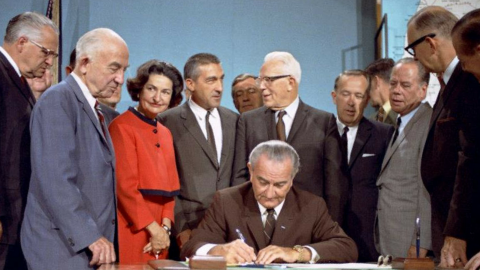Photo of president Lyndon B. Johnson signing document surrounded by legislators and supporters